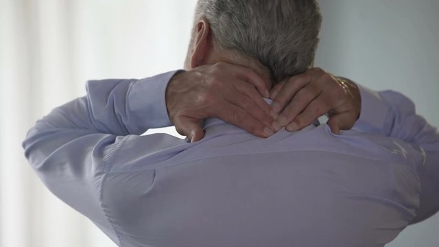 Male employee standing backwards, rubbing back of his neck, office desk worker