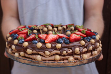 Man holding chocolate cake with strawberries and blueberries