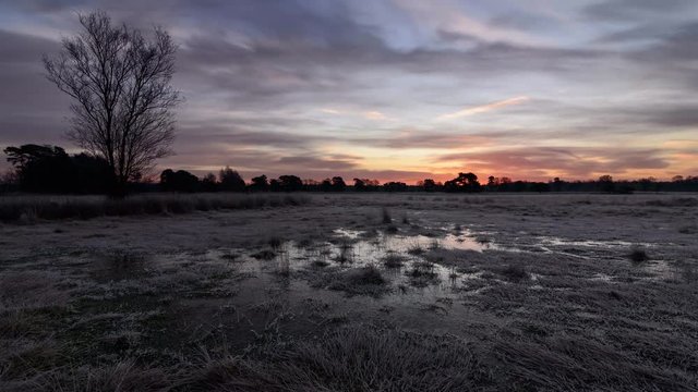 Sunrise over a frozen moor with red clouds reflecting in ice
