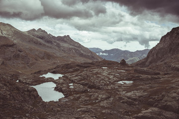 Fototapeta premium High altitude rocky landscape and little lake. Majestic alpine landscape with dramatic stormy sky. Wide angle view from above, toned image, vintage filter, split toning.