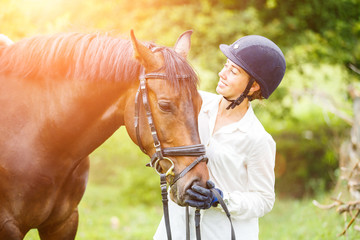 Young beautiful rider woman in helmet holding bay horse by bridle