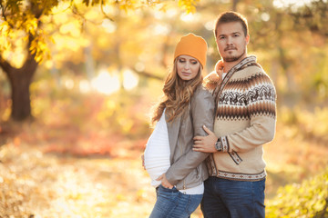 Young happy family have fun and walking in the autumn park. Pregnant woman with husband 