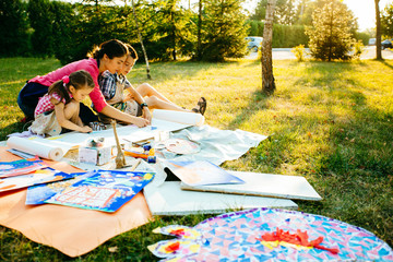 Happy mother, and two kids are painting in the park. The concept of a happy family.