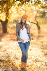 Young pregnant woman in casual clothes walking in autumn park