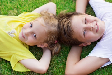 Happy children lying on green grass at backyard