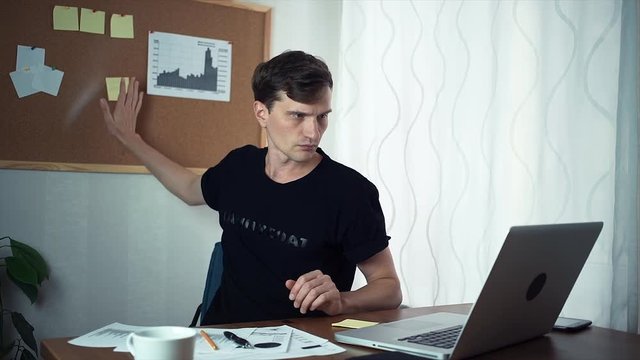 Young man working on laptop computer in the home office. Freelancer writing ideas on adhesive notes and attaching it to board at office