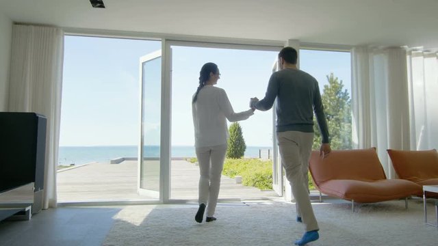 Happy Young Couple Holding Hands and Very Much in Love Run out of Their Home onto the Terrace with Seaside View.  Shot on RED EPIC-W 8K Helium Cinema Camera.