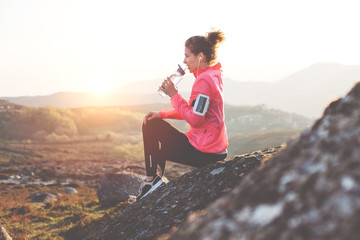 Athletic girl getting ready for a run in the mountains at sunset and drinking water. Sport tight clothes.