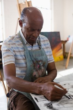 Senior man painting on paper while sitting at table