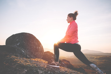 Athletic girl warming up before jogging in the mountains at sunset. Sport tight clothes.