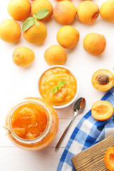 Apricot jam in bowl and glass jar with spoon on white wooden table
