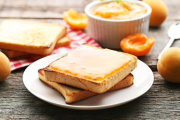 Apricot jam in bowl with bread toasts on grey wooden table