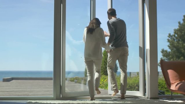Following Shot of a Beautiful Couple Opening Balcony Doors and Walking onto Sunny Terrace with a Seaside View. Sky is Cloudless and People are Happy.Shot on RED EPIC-W 8K Helium Cinema Camera.