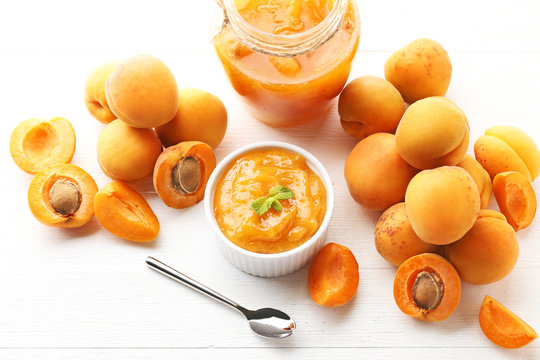 Apricot jam in bowl and glass jar with spoon on white wooden table