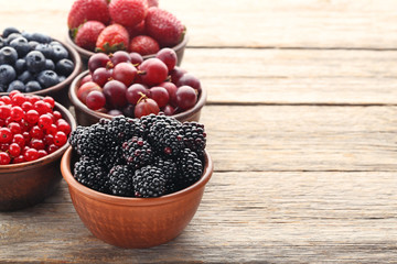 Ripe and sweet berries in bowls on wooden table