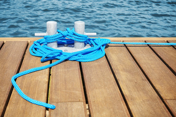 Fototapeta premium Cleat with blue rope on a wooden pier, shallow depth of field.