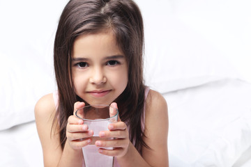 Beautiful little girl drinking water on white bed