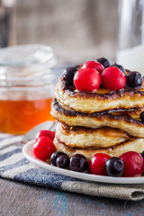 white plate full of pancakes with berries on a wooden background