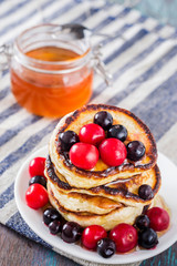 white plate full of pancakes with berries and honey on a wooden background