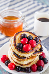 white plate full of pancakes with berries and honey on a wooden background