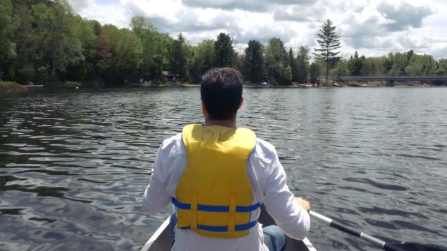 A man rows a boat around Georgian Bay. Cottages and scenery spread out. Medium close up.