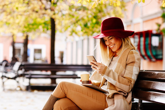 Young woman using smartphone in the city and sitting on the bench