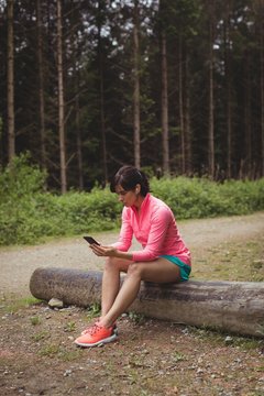 Woman sitting on log and using mobile phone
