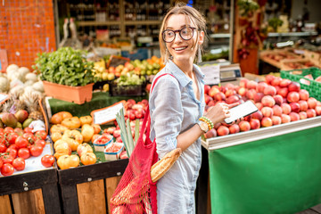 Young woman using smartphone standing with bag in front of the food market in France
