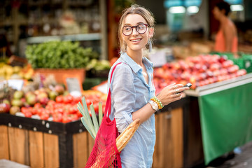 Young woman using smartphone standing with bag in front of the food market in France