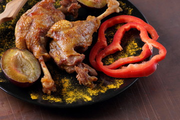 Fried meat with plums and red bell pepper on a black plate with a wooden fork on a rusty background