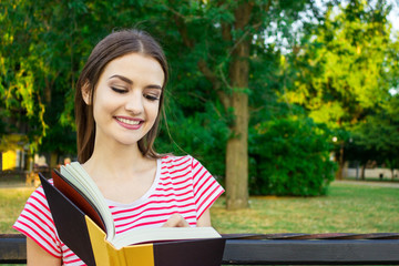 Obraz premium Young smiling woman sitting with diary making some notes in beautiful city park