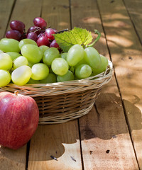 Basket of Grapes and an Apple on a Rustic Wooden Surface