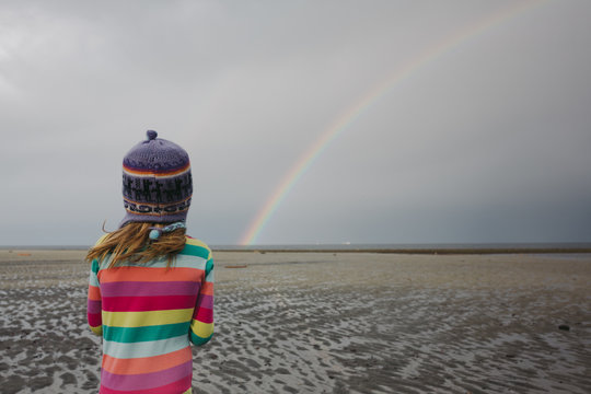 Young caucasian girl chasing rainbow on beach wearing pajamas