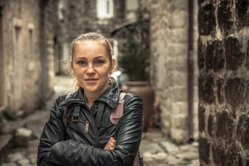 Fototapeta na wymiar Smiling frozen woman standing on narrow medieval street during her travel holidays around Europe in overcast rainy day during autumn