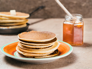 Close up view of homemade pancakes. Stack of pancakes with honey on brown concrete background.