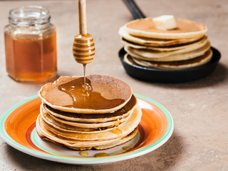 Close up view of homemade pancakes. Stack of pancakes with honey on brown concrete background.