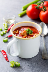 White enamel mug with delicious homemade tomato soup with meatballs and pasta. Healthy food concept.