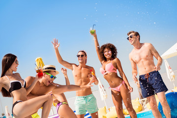 Cropped shot of chilling, dancing international youth, enjoying on resort beach pool sunny disco, in diverse trendy fashionable bikinies, spectacles, caps, with drinks, celebrating holiday