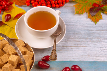 cup of tea with autumn leaves and berries on a rustic wooden background, copy space