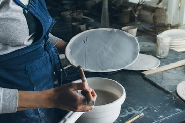 Fototapeta na wymiar Horizontal shot of artist woman holding a clay dish, painting pattern