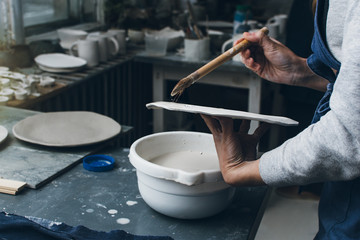 Unrecognizable woman painting a clay dish in pottery studio