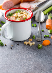Delicious homemade pea soup with sausage and croutons in enamel mug. Healthy food concept with copy space.