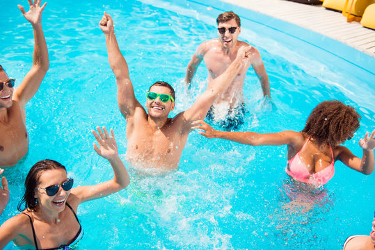 Hands up! Chilling international youth is doing aquaaerobics, enjoying on tourists resort, beach pool sunny disco in the water, in diverse trendy bikinies, spectacles, celebrating holiday dance motion