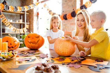 Blonde cute family of mother and two siblings making a jackolantern, boy is taking off the tail of...