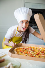 Portrait of young cook woman who standing in the kitchen and sniffing pizza