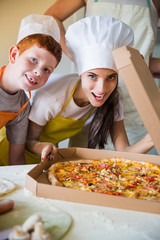 Portrait of young cook woman and her son who standing in the kitchen and sniffing pizza