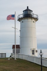 New England lighthouse with American flag standing next to it