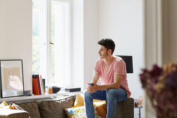 Thoughtful Young Man Holding Coffee Cup On Sofa At Home