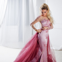 Glamorous lady in a chic pink dress with a train. Studio portrait in white interior