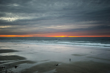 Distant couples stop to view the sunset on a cloudy day at the beach.
